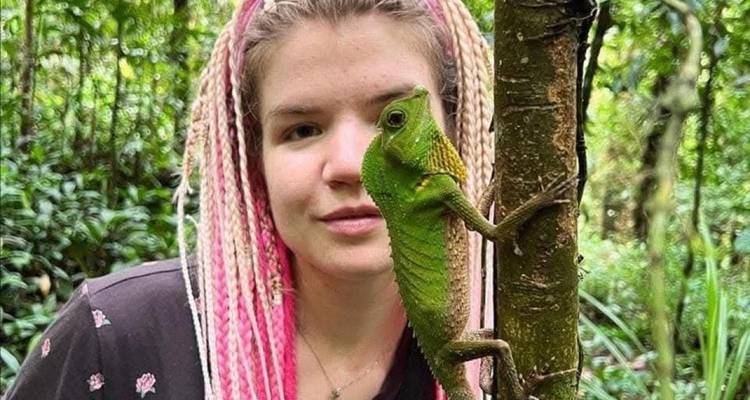 Le voyageur pose à côté d'un caméléon d'un vert vibrant s'accrochant à un tronc d'arbre dans la forêt tropicale.