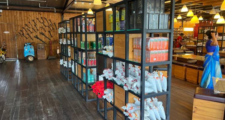 Des étagères de thé emballé et de marchandises bordent un magasin au sol en bois où une femme en sari fait ses achats.