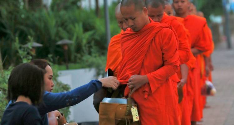 Mönche in orangefarbenen Roben empfangen Opfergaben, möglicherweise in Luang Prabang, Laos.