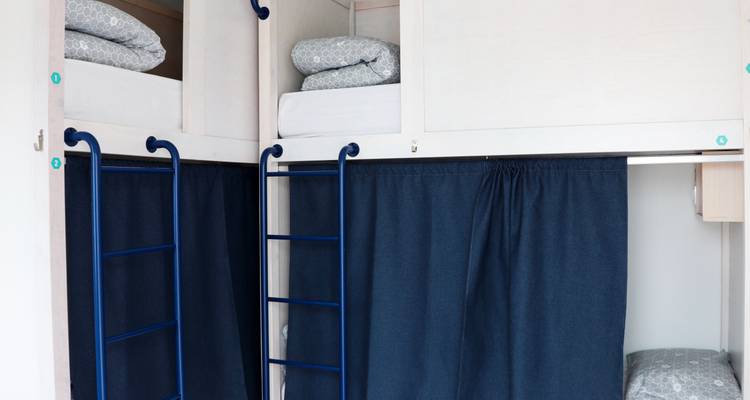 Etagenbetten mit blauen Vorhängen in einer hüttenartigen Umgebung.