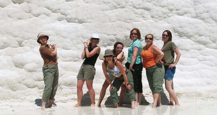 Groep vrouwen die speels poseren in water tot aan hun enkels tegen de witte travertijnwand van Pamukkale.