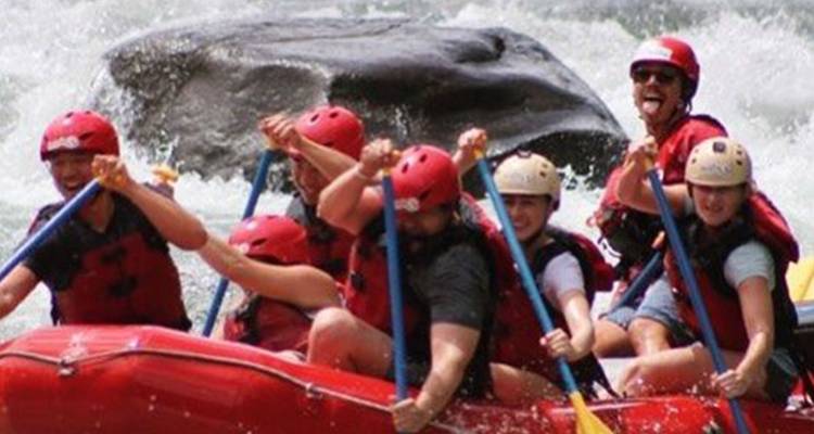 Group of adventurers paddle a red raft through churning white-water rapids