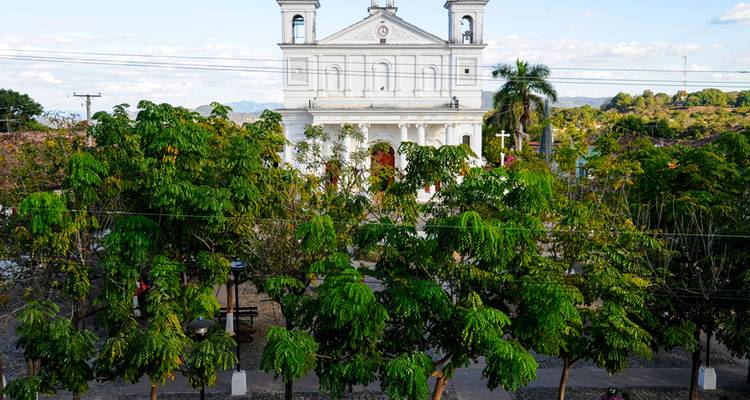 White neoclassical church stands above a leafy plaza in a small colonial town
