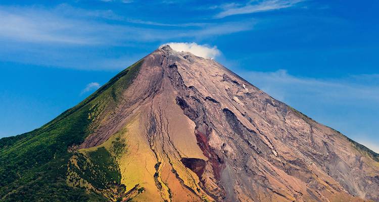 Smoking cone of an imposing stratovolcano rises sharply against a deep blue sky
