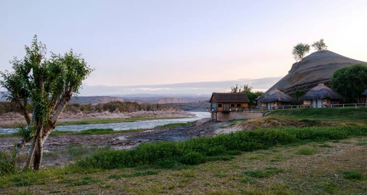Vue pittoresque de la rivière et des collines avec des huttes sur la rive.