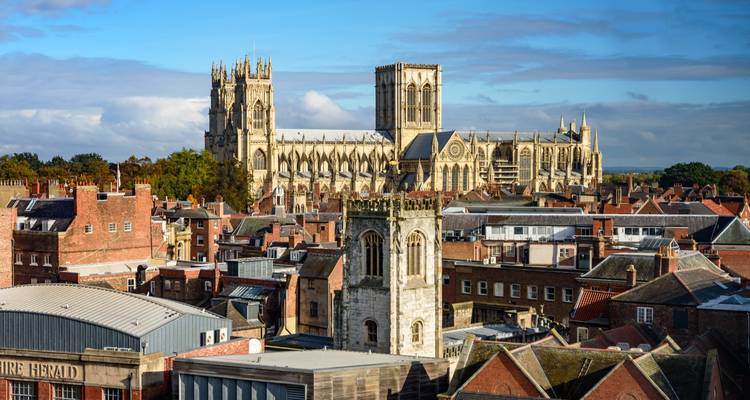 Gothic cathedral dominating a historic city skyline of red-brick rooftops under blue skies.