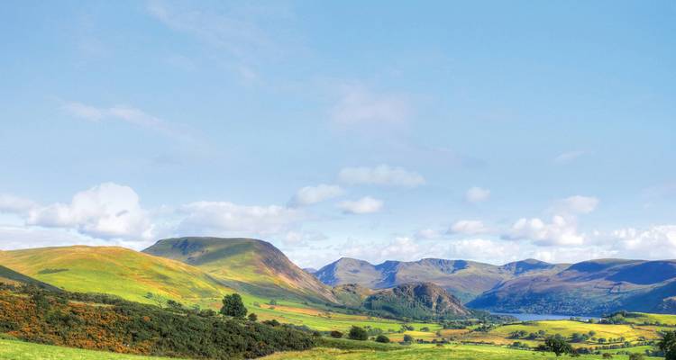 Rolling green hills and valleys of England's Lake District under a bright blue sky.