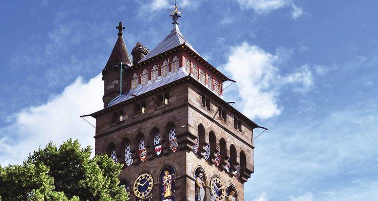 Historic clock tower of Cardiff Castle standing against a blue sky with light clouds.