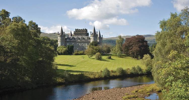 Sprookjesachtige Inveraray Castle gelegen temidden van glooiende Schotse heuvels en weerspiegeld in een rustige rivier.