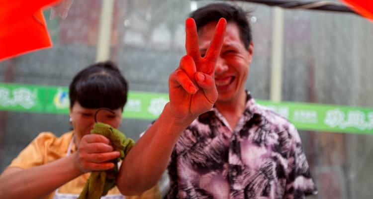 Un hombre sonriente muestra una seña de paz pintada de rojo durante una animada celebración callejera.
