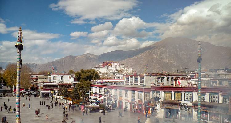 Drukke Barkhor Square in Lhasa met het Potala Palace zichtbaar tegen een achtergrond van bergen.