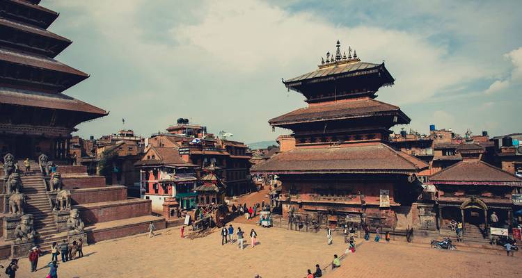 Historisch Bhaktapur Durbar Square met tempels, beelden en bezoekers onder een stralende hemel.
