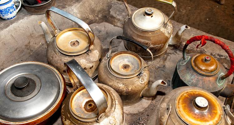 Sammlung von abgenutzten Metallkesseln und Teekannen, die in einem rustikalen Steinwaschbecken stehen.