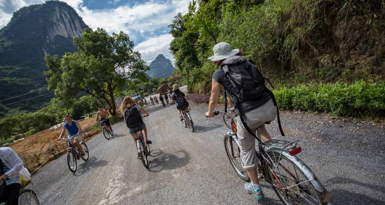 Un grupo de viajeros pedaleando en bicicletas por un camino rural con unos picos de karst bien impresionantes de fondo.
