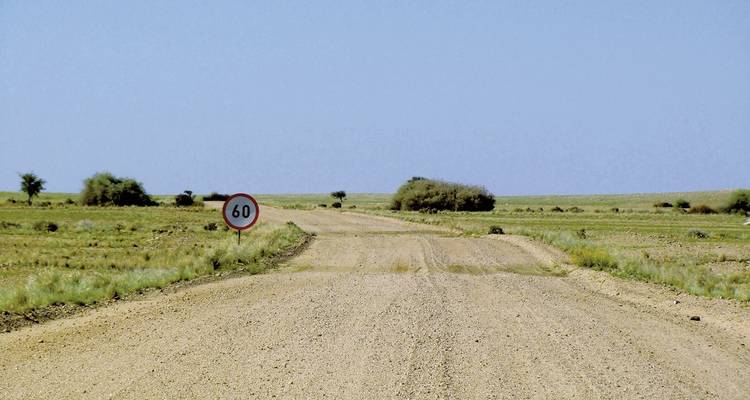 Lange gerade Schotterstraße durch flaches Grasland mit Geschwindigkeitsschild 60 km/h