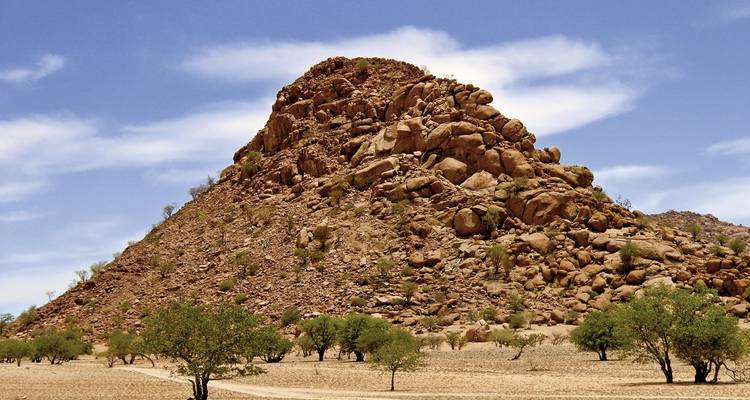 Isolierter Felshügel, der sich über die trockene Savanne mit vereinzelten Akazienbäumen erhebt