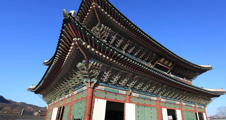 Sala de palacio coreano tradicional con aleros pintados ornamentados bajo un cielo azul profundo.