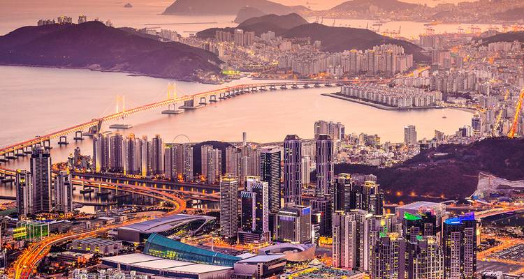 Vista panorámica al atardecer del horizonte de Busan y el puente Gwangan iluminado que atraviesa la bahía.