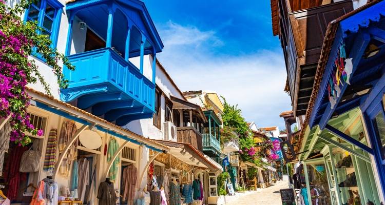 Las tiendas boutique coloridas se alinean en una calle empedrada y soleada adornada con buganvilia y balcones brillantes.