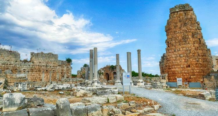 Ruinas antiguas romanas con columnas dispersas y muros de piedra desgastados bajo un cielo brillante.