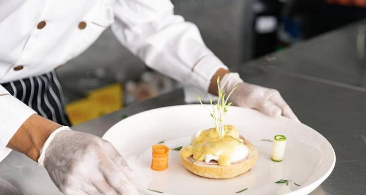 Koch richtet ein Gericht mit Eggs Benedict in einer Küchenumgebung an.