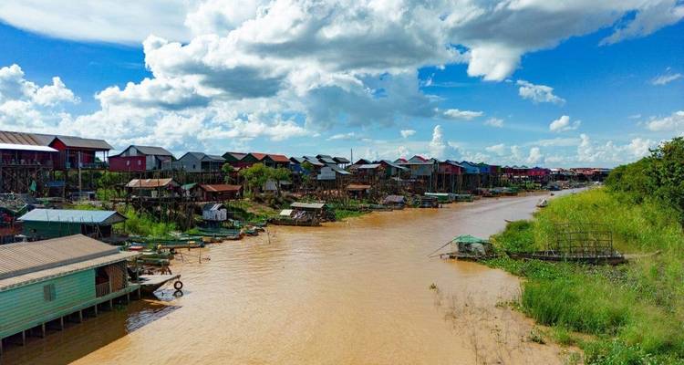Village houses along a muddy river under a blue sky.