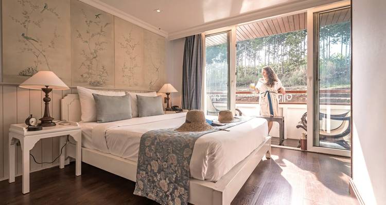 Elegant bedroom with a person on a balcony on a river cruise ship.