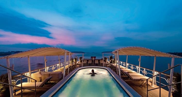 Person swimming in a pool on a river cruise ship at dusk.
