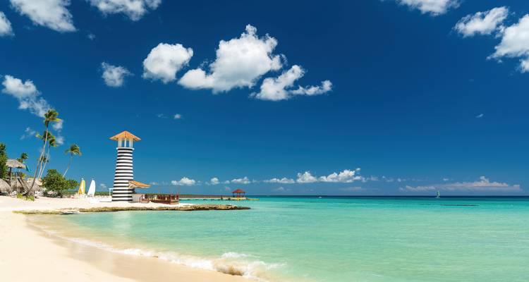 Tropischer Strand mit türkisblauem Wasser und einem Leuchtturm.