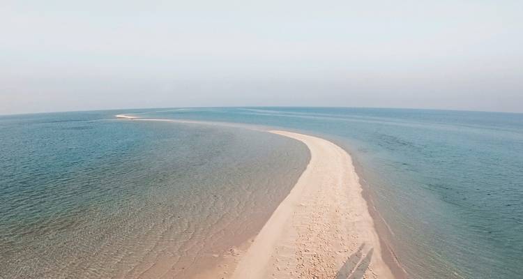 Luftaufnahme einer Sandbank, die sich ins Meer erstreckt.