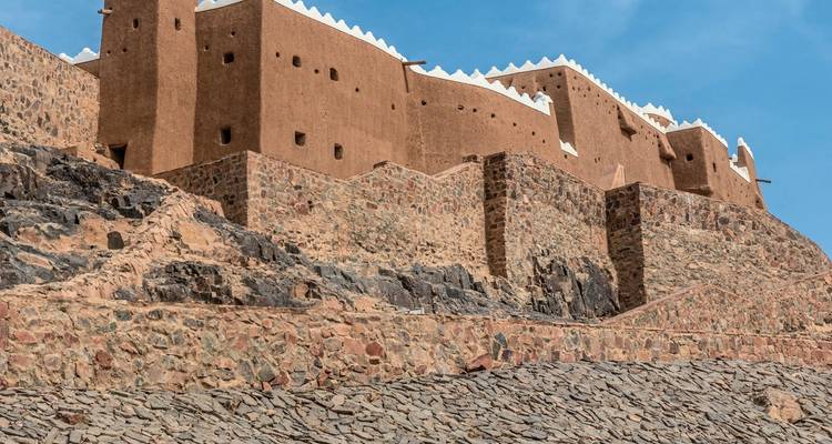Historic mud-brick fortress with stone foundations against a clear blue sky.