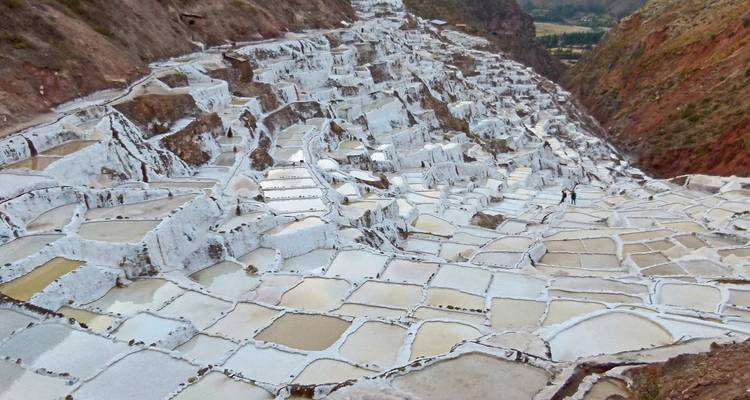 Terrassenförmige Salzpfannen in einem Tal mit einigen arbeitenden Menschen.