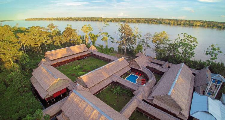 Luftaufnahme eines Resorts mit Pool an einem Fluss, umgeben von üppigem Wald.
