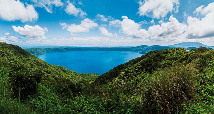 Large lake surrounded by forested hills under a bright sky.