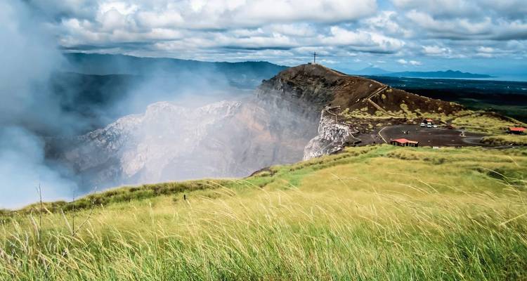 Scenic volcanic crater with rising smoke and surrounding hills.
