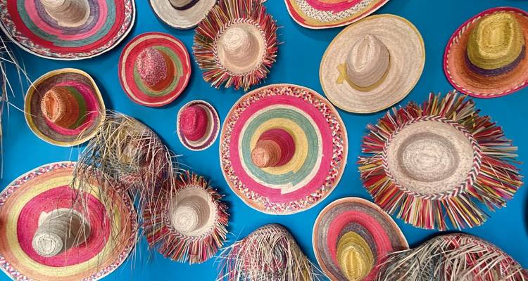 Des chapeaux de paille colorés exposés sur un mur bleu.