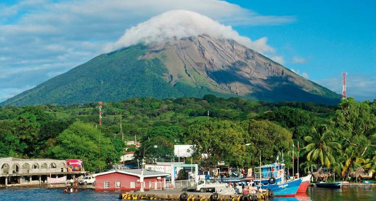 Volcan avec sommet couvert de nuages et village coloré au bord de l'eau.