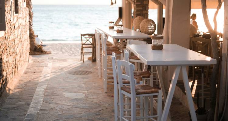 Bar extérieur en bord de mer avec des tabourets hauts sous la lumière chaude du coucher de soleil près du rivage.