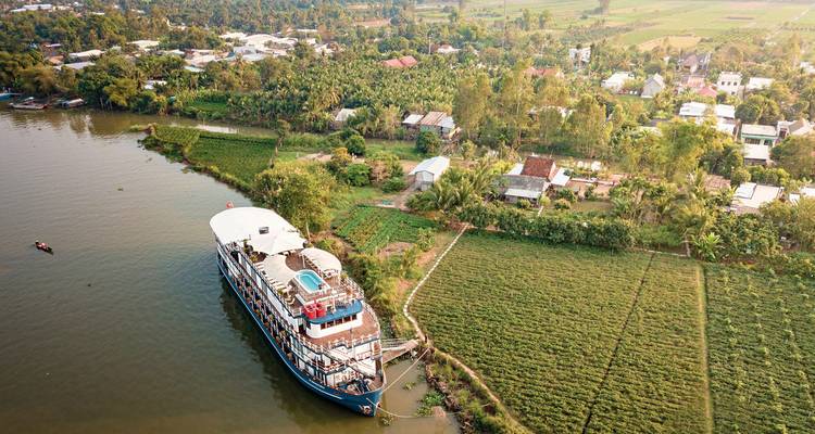 Flusskreuzfahrtschiff an einem ländlichen Flussufer mit Dorfblick.