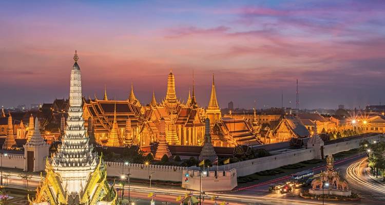 Paisaje urbano de Bangkok con templos iluminados al anochecer.