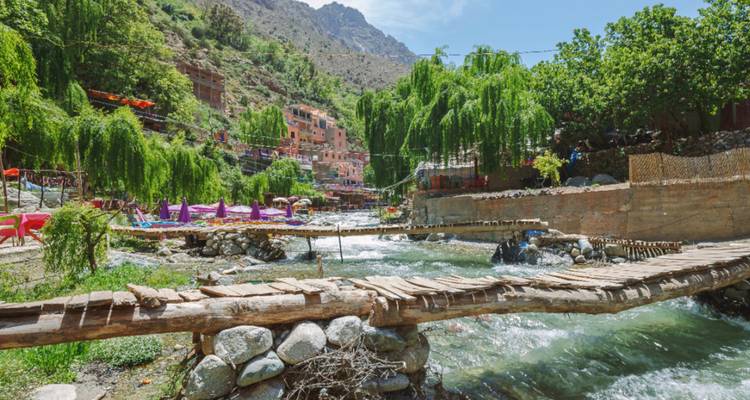 Riverside cafés and wooden footbridges along a fast-flowing stream in a mountain village.