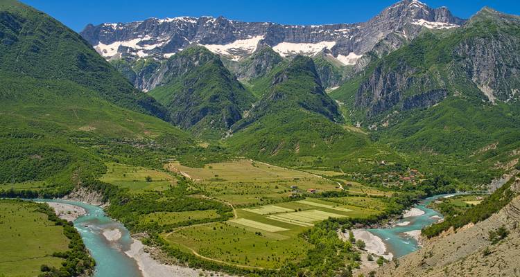 Vista panorámica de un río turquesa sinuoso que atraviesa un exuberante valle albanés bajo picos dentados.
