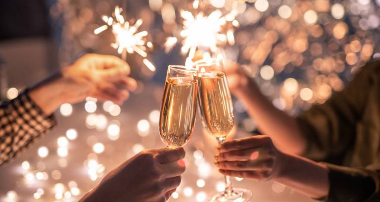 Handen die champagneglazen met sparklers tegen elkaar tikken en feestelijke bokeh-lichtjes creëren.