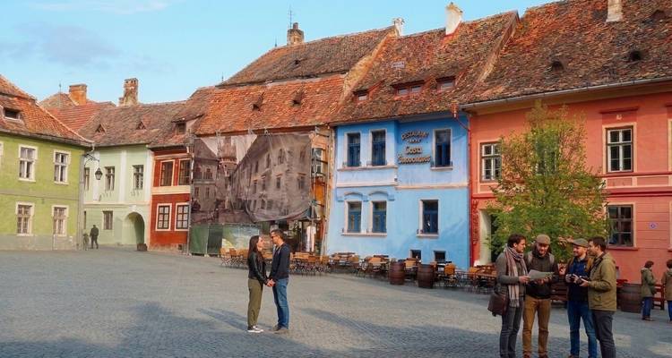 Des maisons médiévales colorées bordent une place pavée de galets où de petits groupes de visiteurs discutent à la lumière du soir.