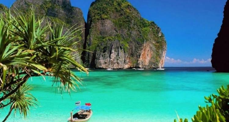 Tranquil view of a boat docked in a turquoise bay surrounded by rocky cliffs.