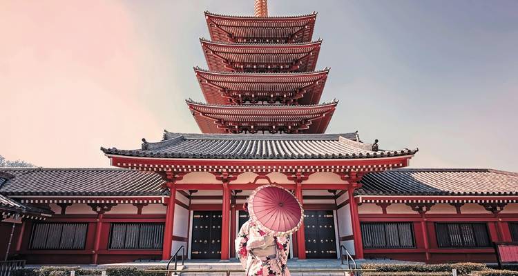 Frau in traditionellem Kimono mit Regenschirm an einem Tempel.