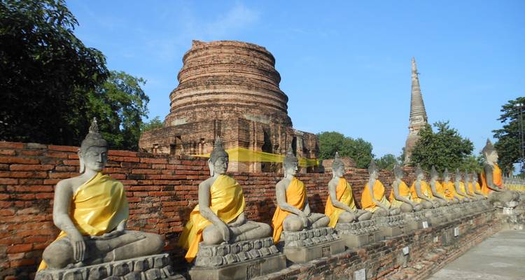 Antike Ziegelstupa mit einer langen Reihe von sitzenden Buddhafiguren in gelben Gewändern an einer historischen Stätte.