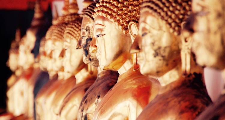 Reihe von vergoldeten Buddha-Statuen in einem Tempelkorridor, sanft beleuchtet mit warmen Tönen.