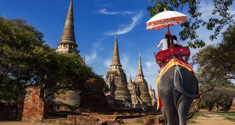Eine Person, die auf einem Elefanten zu historischen Pagoden reitet.