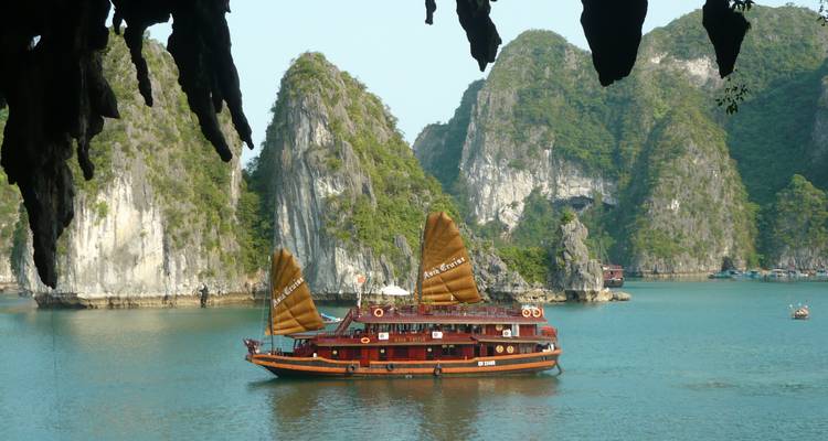 Ein traditionelles Dschunkenboot, das auf klarem blauem Wasser segelt, umgeben von Kalksteinkarst.